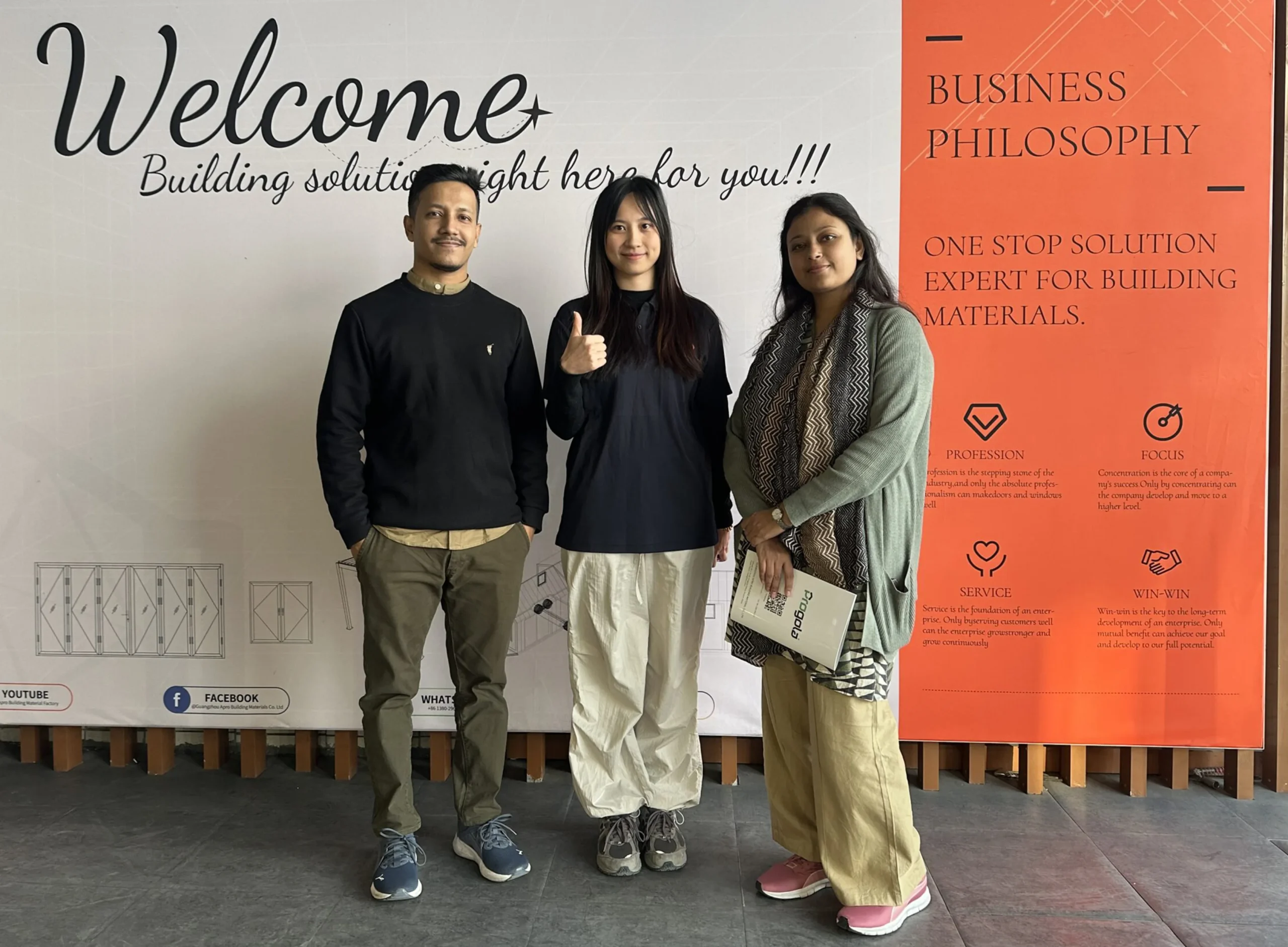 A photo of Progolas & Aprodoor's salesperson and Southeast Asian clients in front of the company's billboard