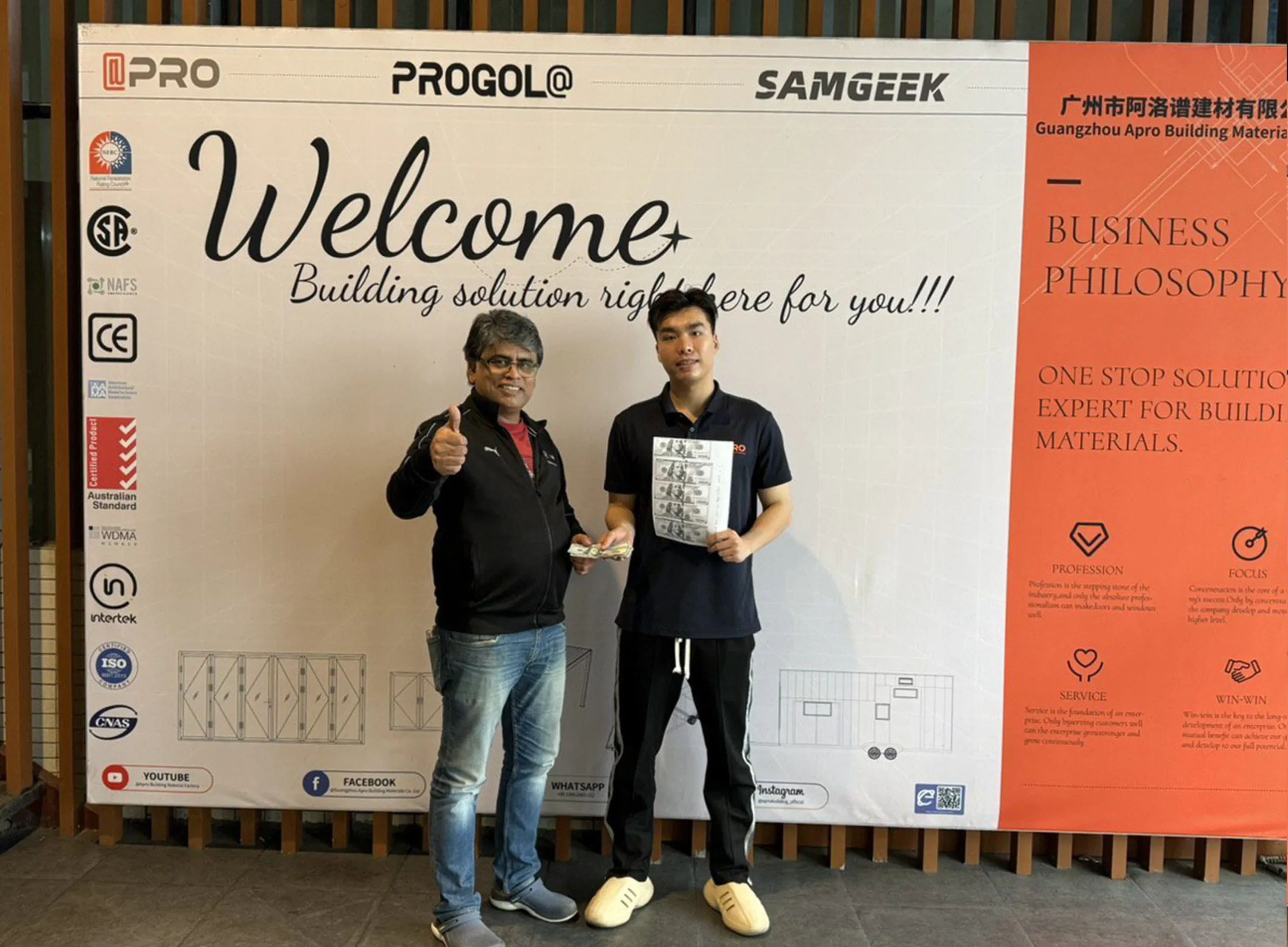 Progolas & Aprodoor salesmen chirs and South Asian clients take a photo in front of the company's billboard
