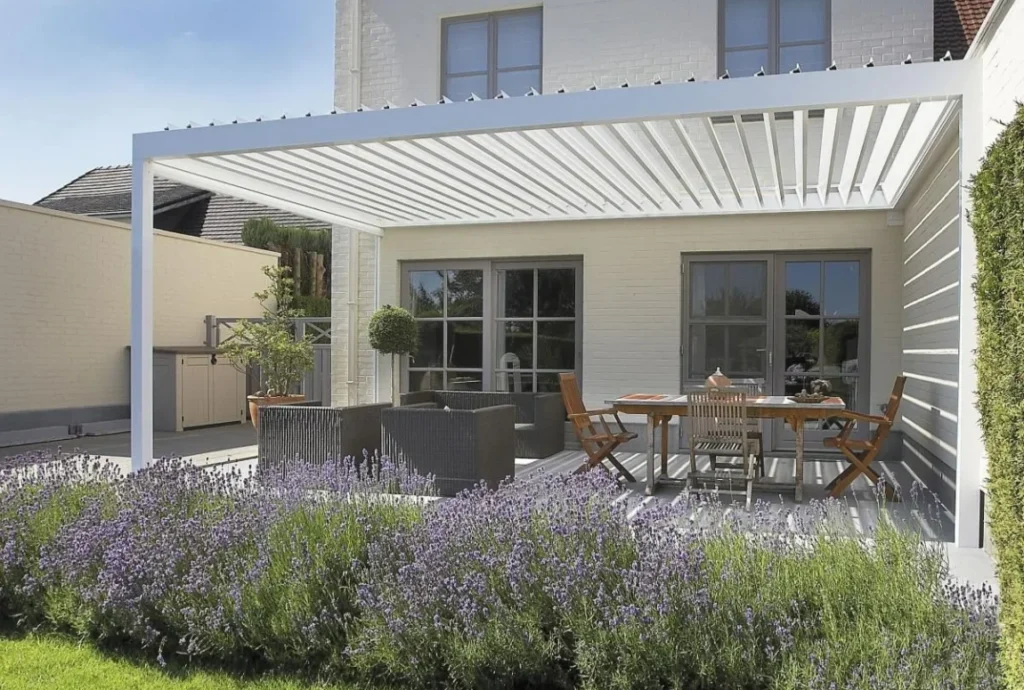 집 뒷문에 흰색 1410 시리즈 전동 어닝이 설치되어 있고, 그 아래에 식탁과 의자가 놓여 있다.